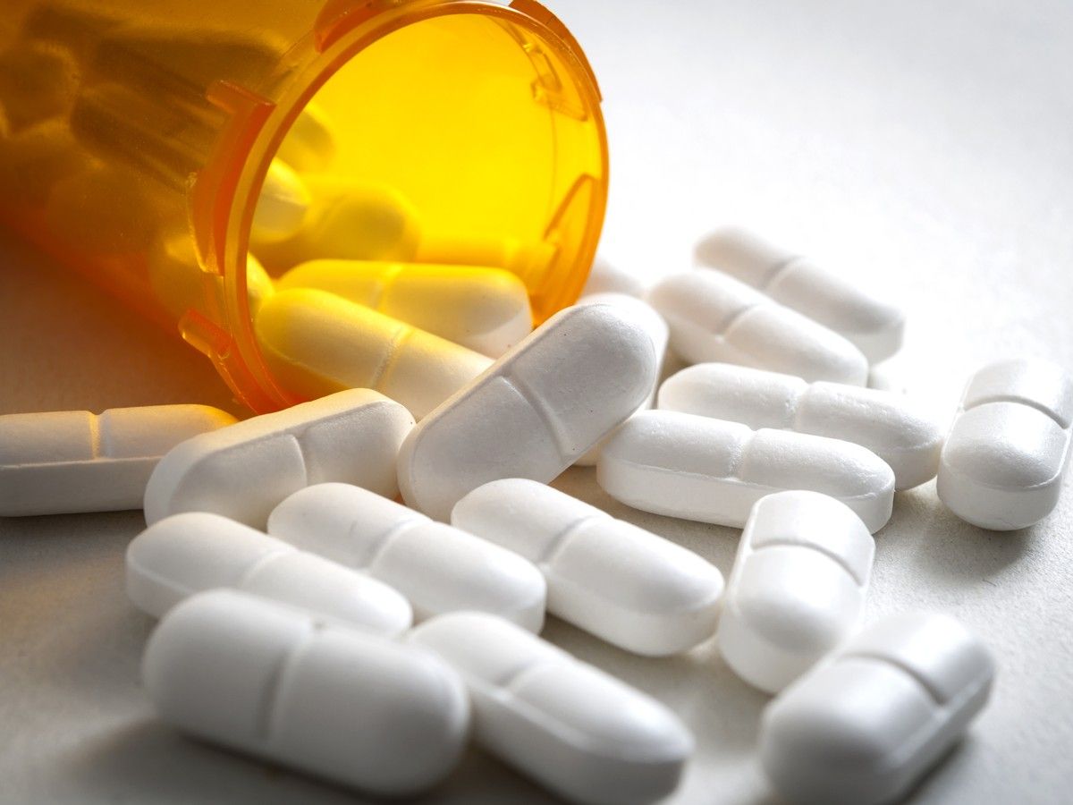 White pills next to an orange pill bottle on a white background.