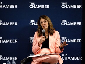 Danielle Smith in a pink suit holding a microphone while sitting down.