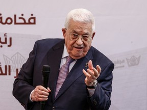 Palestinian President Mahmoud Abbas in a suit holding a microphone.