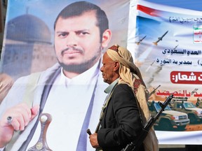 A fighter loyal to the Houthi authorities, walks past a poster bearing a picture of his group's leader Abdul-Malik al-Houthi