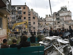 Local residents look at rescuers working on a multi-floor residential building destroyed