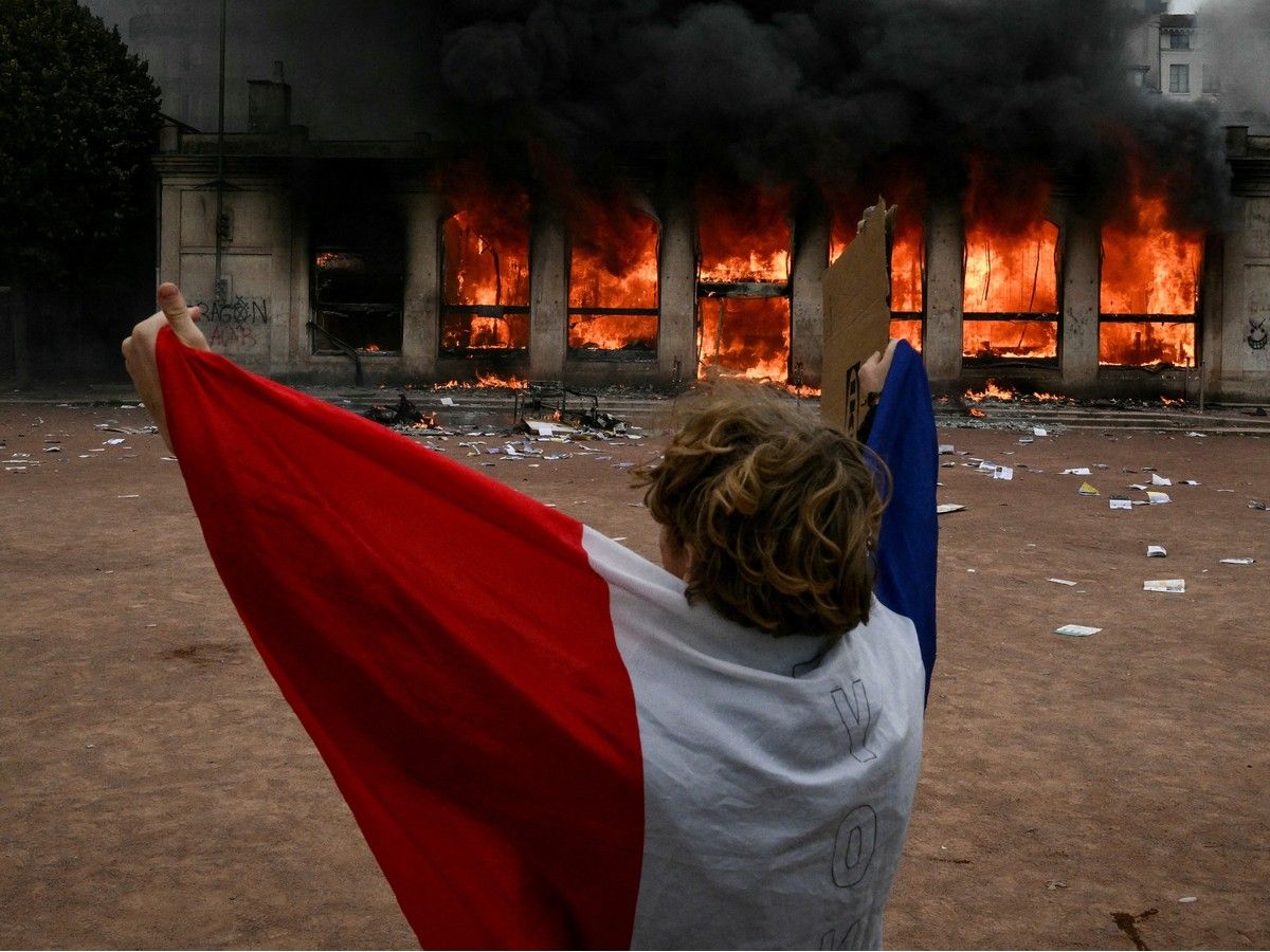 A protester wrapped in a French national flag stands in front of Lyon's tourism office set on fire