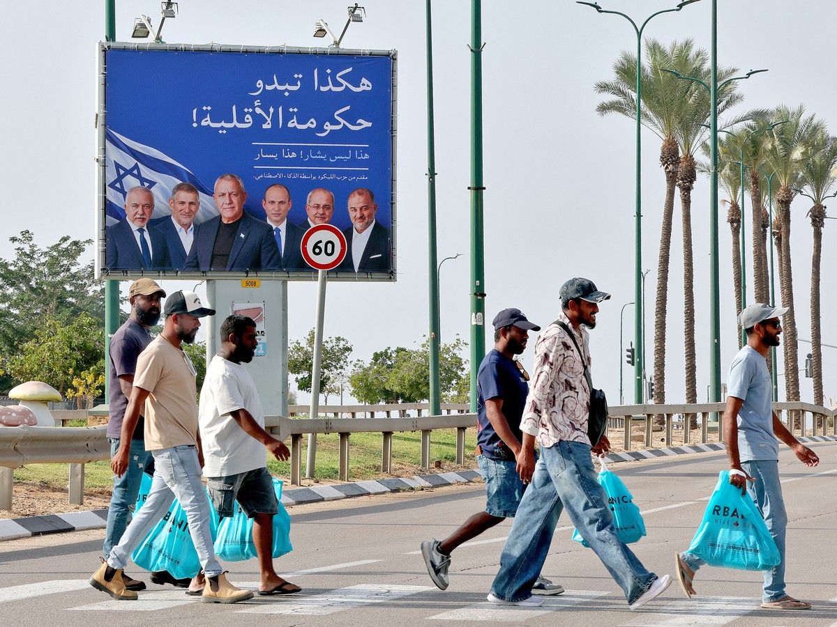 Pedestrians cross a road in front of an electoral banner for Israeli Prime Minister Benjamin Netanyahu.