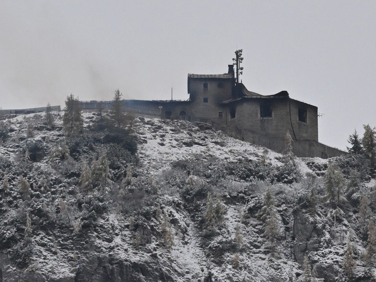 Smoke outside a building on top of a snowy hill under a grey sky.