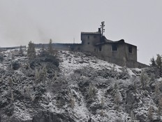 Smoke outside a building on top of a snowy hill under a grey sky.