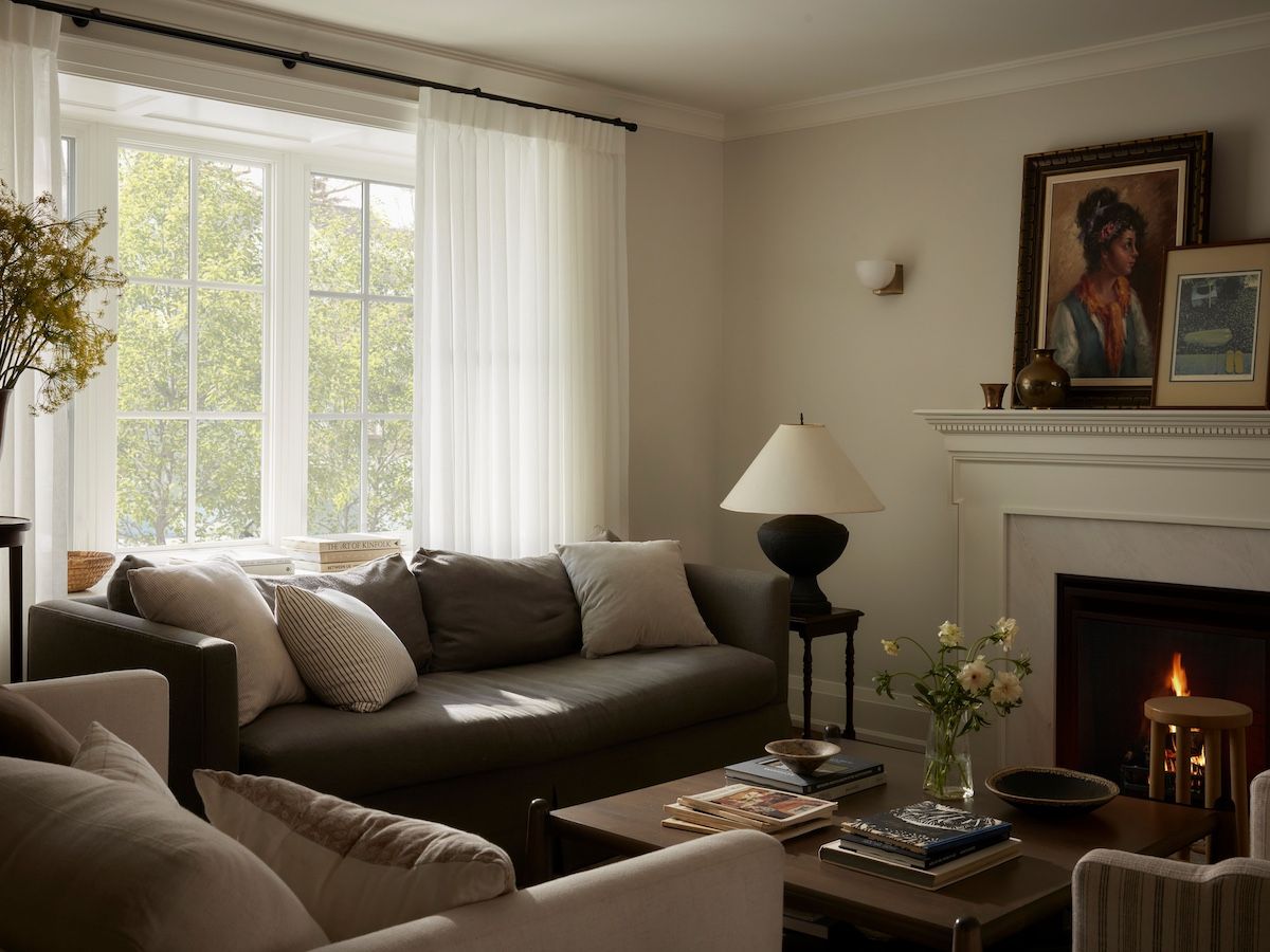 Custom sheer draperies let in filtered light to the living room, adding to the air of comfort produced by sink-into furnishings, old family pieces (the side table at right has been in the family for generations), and art casually propped on the mantel.