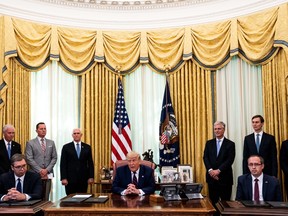 Donald Trump sits at a table in the Oval Office with President of Serbia Aleksandar Vucic (L) and the Prime Minister of Kosovo Avdullah Hoti (R) sat beside him.