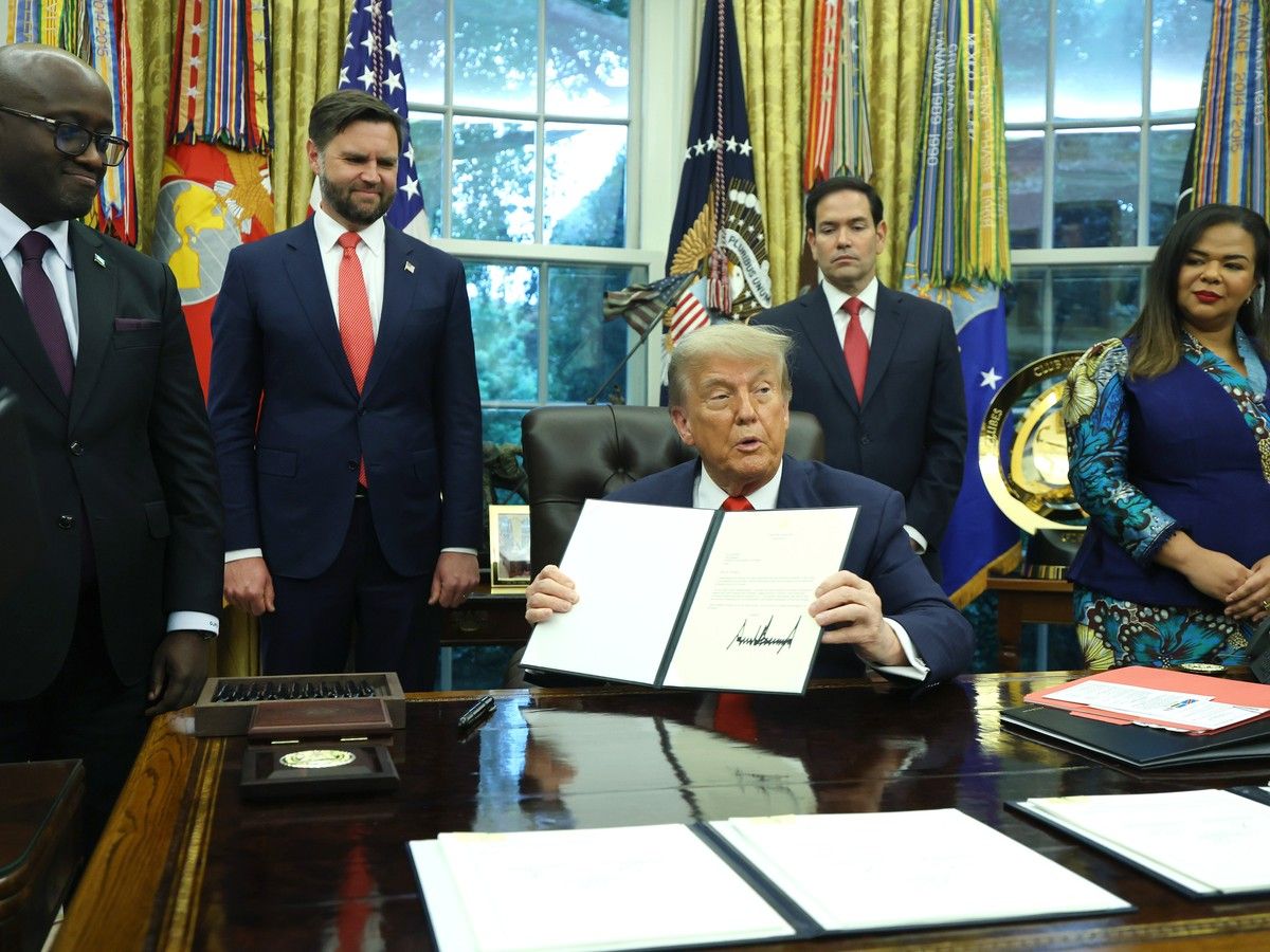Donald Trump holds up a signed letter in the oval office while Minister of Foreign Affairs and Cooperation of Rwanda Olivier Nduhungirehe and the Foreign Minister of the Democratic Republic of the Congo Thérèse Kayikwamba Wagner stand either side.