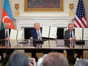 President Donald Trump (C), Azerbaijani President Ilham Aliyev (L), and Armenian Prime Minister Nikol Pashinyan (R) each hold up a signed agreement while sat at a table in the White House.