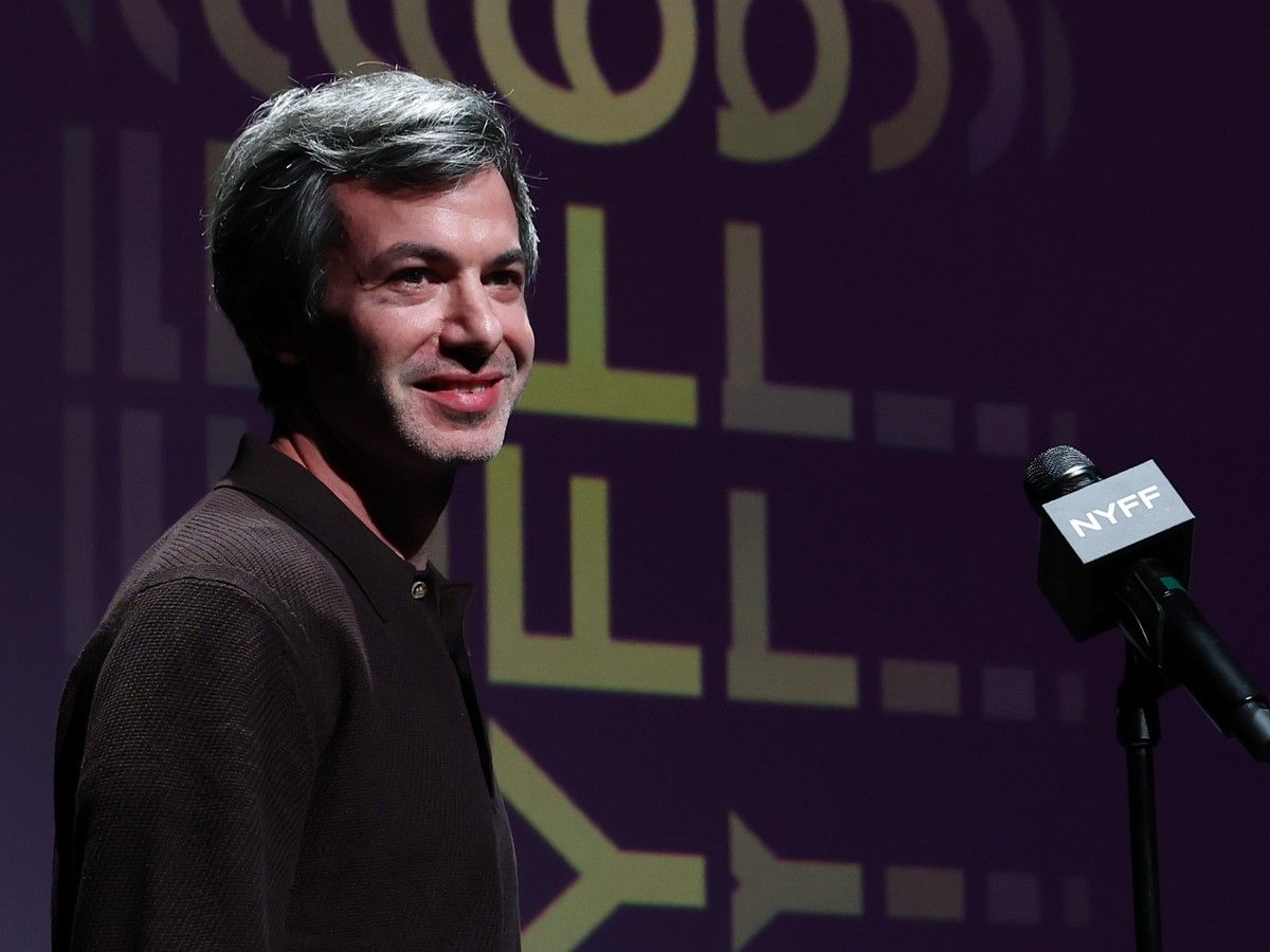 Nathan Fielder smiles while standing on stage next to a microphone.