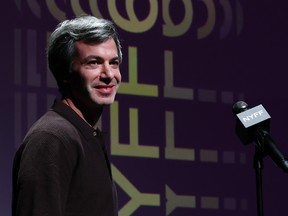 Nathan Fielder smiles while standing on stage next to a microphone.
