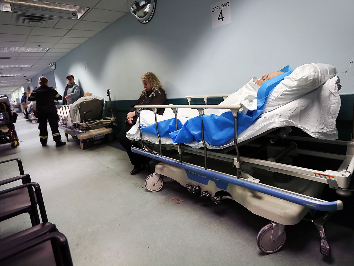 Hospital patients on beds in a hallway.