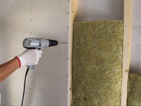 Close-up of worker hand with electric screwdriver fastening drywall to wooden timber frame with insulation mineral rock wool staff. Warm home, low energy bills, construction and renovation concept.