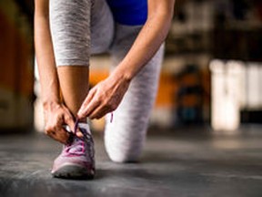 stock-photo-woman-tying-her-shoe-in-an-open-empty-gym-preparing-for-workout-or-run-wearing-gray-leggings-and-1065946166