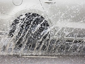 Car motion through big puddle of water splashes from the wheels on the street road.