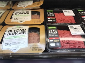 Packages of hamburger patties, made from the plant-based simulated meat product Beyond Meat, sit next to lean ground beef in the meat section of a grocery store.