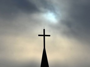 The sun is obscured by clouds behind the steeple and cross of a  church in this file photo.