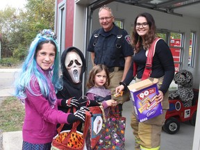 Blenheim residents Olivia MacDonald, 9, left, and her siblings Carter, 6, and Sophia, 5, receive treats from Harwich Station No. 12 firefighters Dennis Dath and Helen Grubb, during the annual safe Halloween event, held at the Chatham-Kent Children's Safety Village on Saturday, located at the C.M. Wilson Conservation Area Saturday. (Ellwood Shreve/Chatham Daily News)