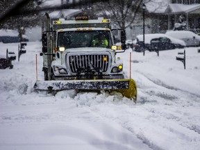 White snowplow service truck with orange lights and yellow plow blade clearing residential roads of snow while flakes are still falling
