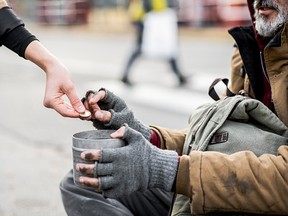 A midsection view of woman giving money to homeless beggar man sitting in city.