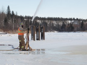 A construction worker sprays water to build up ice thickness on the Firebag River along the winter ice road from Fort McMurray to Fort Chipewyan on February 4, 2015. Ryan Jackson/Postmedia Network