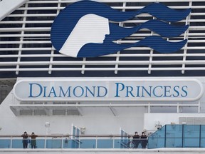 Masked passengers look on from onboard the coronavirus-hit Diamond Princess cruise ship docked at Yokohama Port, south of Tokyo, Japan, on Feb. 20.