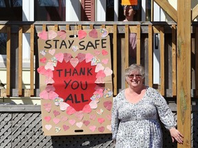 Sue Kirkland stands next to a poster she created with the help of her daughter, Sarah, who is looking out of the door window at their home in Sudbury, Ont.