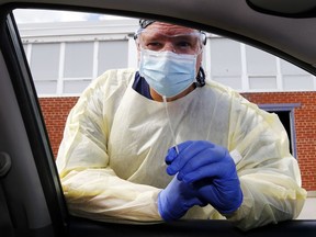 Hastings-Quinte paramedic Scott Bennett leans into a vehicle while holding a testing swab at the COVID-19 assessment centre in Belleville.