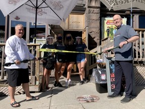 Brockville Mayor Jason Baker, left, and local MPP Steve Clark use specially-purposed hockey sticks to cut the ribbon on the Keystorm Pub Friday morning to celebrate the region's gradual reopening from COVID-19 restrictions. Joining them, from left, are Keystorm employees Amanda Toohey, Erica Bulanda, Madison Henderson and Paige Gleason. (RONALD ZAJAC/The Recorder and Times)