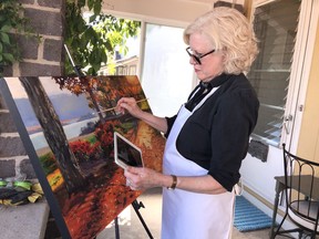 Pam Warren Mckinnon, one of the participants in Saturday's Brockville edition of the National Arts Drive, paints a Hardy Park scene on the porch of her Water Street home, from where she will be showing her work. (RONALD ZAJAC/The Recorder and Times)