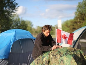 Nathan Rosevear attaches a Canadian flag to his tent at Belle Park on Sunday. (Meghan Balogh/The Whig-Standard)