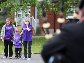 Mary Hodgins, right, stands with her daughter and grandson as piper Ross Brown leads a procession of friends and supporters past the Hodgins home on Saturday. (Meghan Balogh/The Whig-Standard)