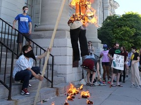 Protesters burned an effigy of Sir John A. Macdonald on the steps of Kingston City Hall on Saturday. More than 100 people marched along King Street to demand that the municipality remove the statue of Sir John A. Macdonald from City Park. (Meghan Balogh/The Whig-Standard)