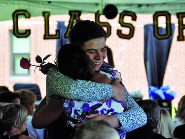 J.T. Foster graduate Dallon Southgate gives mom Brenda a hug after presenting her with a rose during a graduation ceremony Saturday afternoon. The school held three separate graduation ceremonies under a tent on the lawn north of the school to keep each of the outside gatherings under total 100 people, the current maximum the Alberta government is allowing.