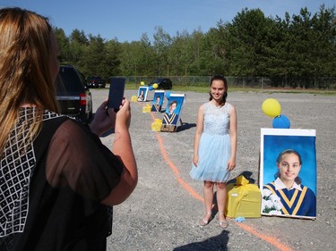 Graduating student Hailey Robillard, 13, poses for a picture, as her mom, Alishea, takes photos near Hailey's picture at St. Anne Catholic School's Grade 8 drive-thru graduation ceremony in Hanmer, Ont. on Wednesday June 17, 2020. More than 50 graduating students and their families took part in the ceremony. John Lappa/Sudbury Star/Postmedia Network