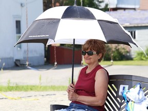In this file photo, Helen Mayer uses an umbrella to protect herself from the sun and heat while visiting the splash pad at the DJ Hancock Memorial Park with her grandson.