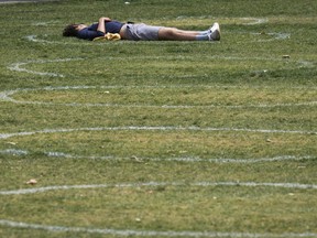 A person lays on the grass in a circle drawn to promote physical distancing.