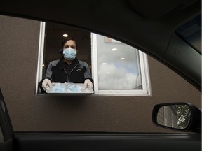 An employee at the 7455 101 Avenue A&W location poses for a photo with packages of non-medical masks in the restaurant's drive-thru, in Edmonton Monday June 8, 2020. In an effort to prevent the spread of COVID-19 the Province is distributing 20 million free, non-medical face masks through A&W, McDonald's, and Tim Hortons drive-thrus. Photo by David Bloom