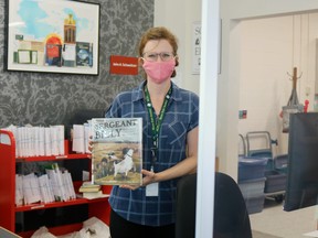 Katie McNamara, library assistant at the Delhi Branch of the Norfolk County Public Library, stands behind a sneeze guard at the front desk while wearing a mask as part of the COVID-19 emergency response. (ASHLEY TAYLOR)