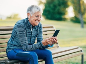 Senior sportswoman with smart phone and headphones sitting in the park.