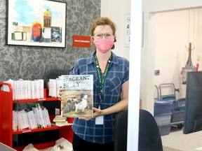 Katie McNamara, library assistant at the Delhi branch of the Norfolk County Public Library, stands behind a sneeze guard at the front desk while wearing a mask as part of the COVID-19 emergency response. Ashley Taylor photo
