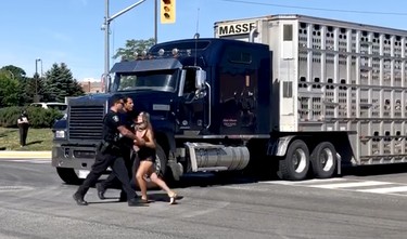 Halton Regional police remove activist Sabrina Desgagnes after she walked into the intersection in front of a moving transport attempting to entering the Sofina Fearman's Pork Ltd. processing plant in Burlington on a green light and right-of-way, July 30, 2020. Desgagnes repeated this action several times over the course of the protest.