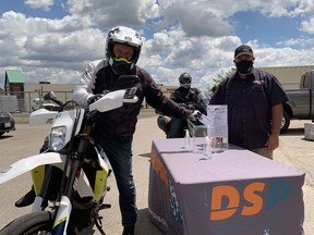 Doug Hunt, of Participation Support Services, demonstrates how to do a COVID-safe drive-by drop-off for this year's motorcycle run in support of Participation Support Services and the Brant, Haldimand, Norfolk branch of the Canadian Mental Health Association. Hunt is putting a riding identification card in the box. The boxes will be collected by organizers following the event and names will be drawn for prizes. Hunt is joined by Brent Goodnough, of the Brant, Haldimand, Norfolk branch of the Canadian Mental Health Association, and Clint MacBride, of DualSport Plus, in Brantford. Vincent Ball
