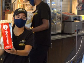 A masked Landmark Cinemas employee hands popcorn to customers after the Alberta government lifted COVID-19 restrictions that had forced theatres to close in March 2020. Movie theatres in Alberta were allowed to reopen in June. Supplied Image/Landmark Cinemas
