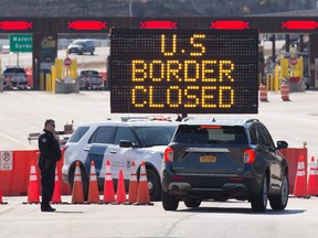 In this file photo US Customs officers speak with people in a car beside a sign saying that the US border is closed at the US/Canada border in Lansdowne, Ontario, on March 22, 2020. (FILE PHOTO)