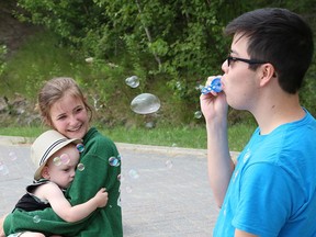 Tanner Webkamigad entertains Janelle Cloutier and her nephew, Benjamin Berthiaume, 14 months, by blowing soap bubbles at Bell Park in Sudbury, Ont. on Wednesday July 15, 2020.
