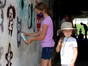 Molly Johnston paints graffiti in the CN Tunnel in Stony Plain Thursday, July 30, 2020 while Theodora Goetz watches. In the background is her sister Sadie Johnston. The Town is currently hosting a series of workshops on the medium that is set to conclude later this month.