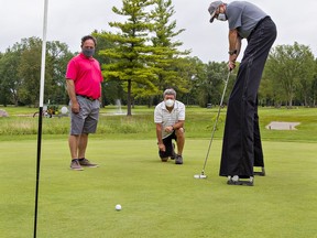 Golf pro Paul Mikelbrencis (left) and organizing committee member Cort Stubbert watch as Brantford's world record-holding stilt walker Doug Hunt makes a putt at Burford Golf Links.