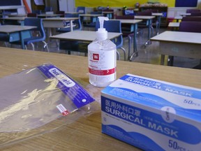 Faceshields, hand sanitizer and masks sit ready on a teacher's desk in a classroom.
