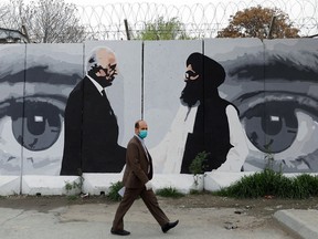An Afghan man wearing a protective face mask walks past a wall painted with graphic of Zalmay Khalilzad, left, U.S. envoy for peace in Afghanistan, and Mullah Abdul Ghani Baradar, the leader of the Taliban delegation, in Kabul, Afghanistan, on April 13, 2020. The pair had signed an agreement at a ceremony between members of Afghanistan's Taliban and the U.S. in Doha, Qatar, on Feb. 29, 2020. (Mohammad Ismail/Reuters)